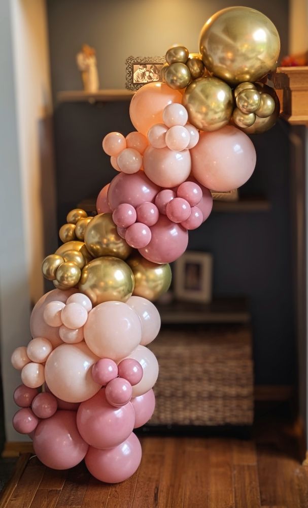 Balloon arch in shades of pink and gold, cascading down from a shelf.