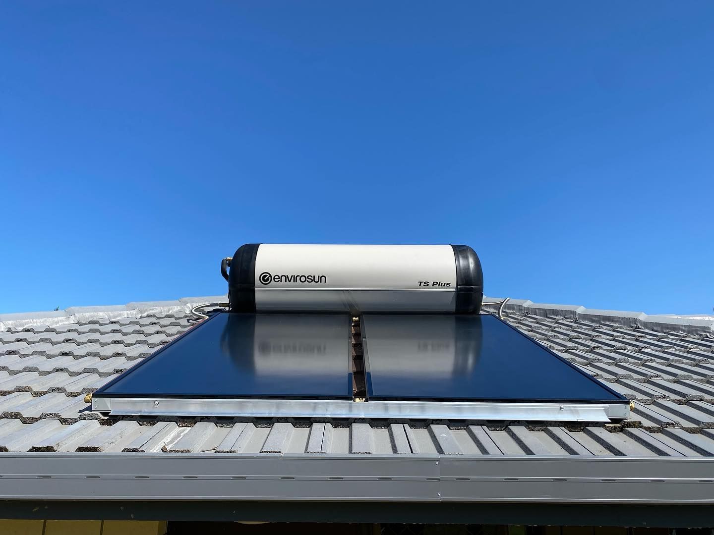 Solar water heater on a tiled roof under a clear blue sky.