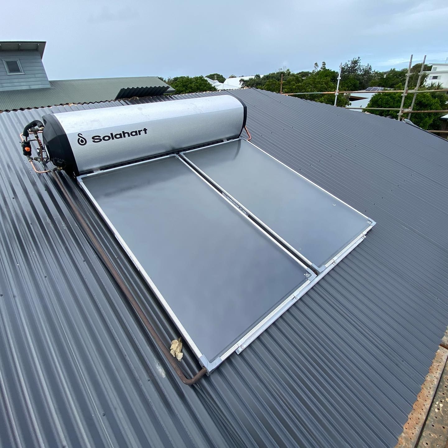 Solar water heater on a gray corrugated metal roof, with two rectangular panels and a silver tank.