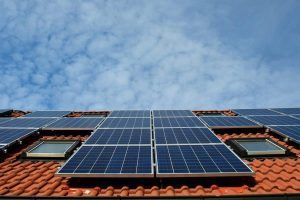 Solar panels on a red-tiled roof against a cloudy blue sky.