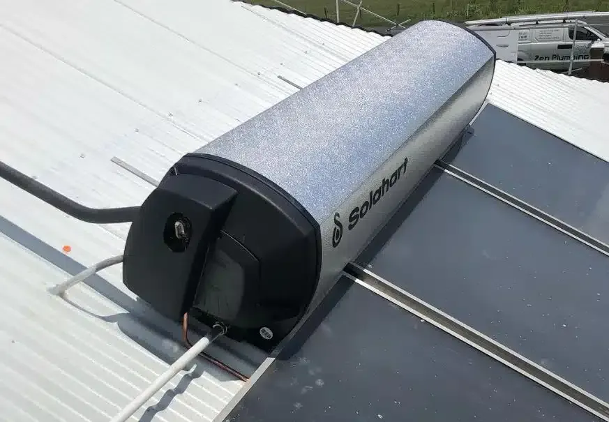 Solar hot water tank on a roof, next to solar panels. Silver tank with black ends.
