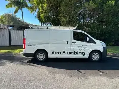 White Zen Plumbing van parked on a street with a blue sky and trees in the background.