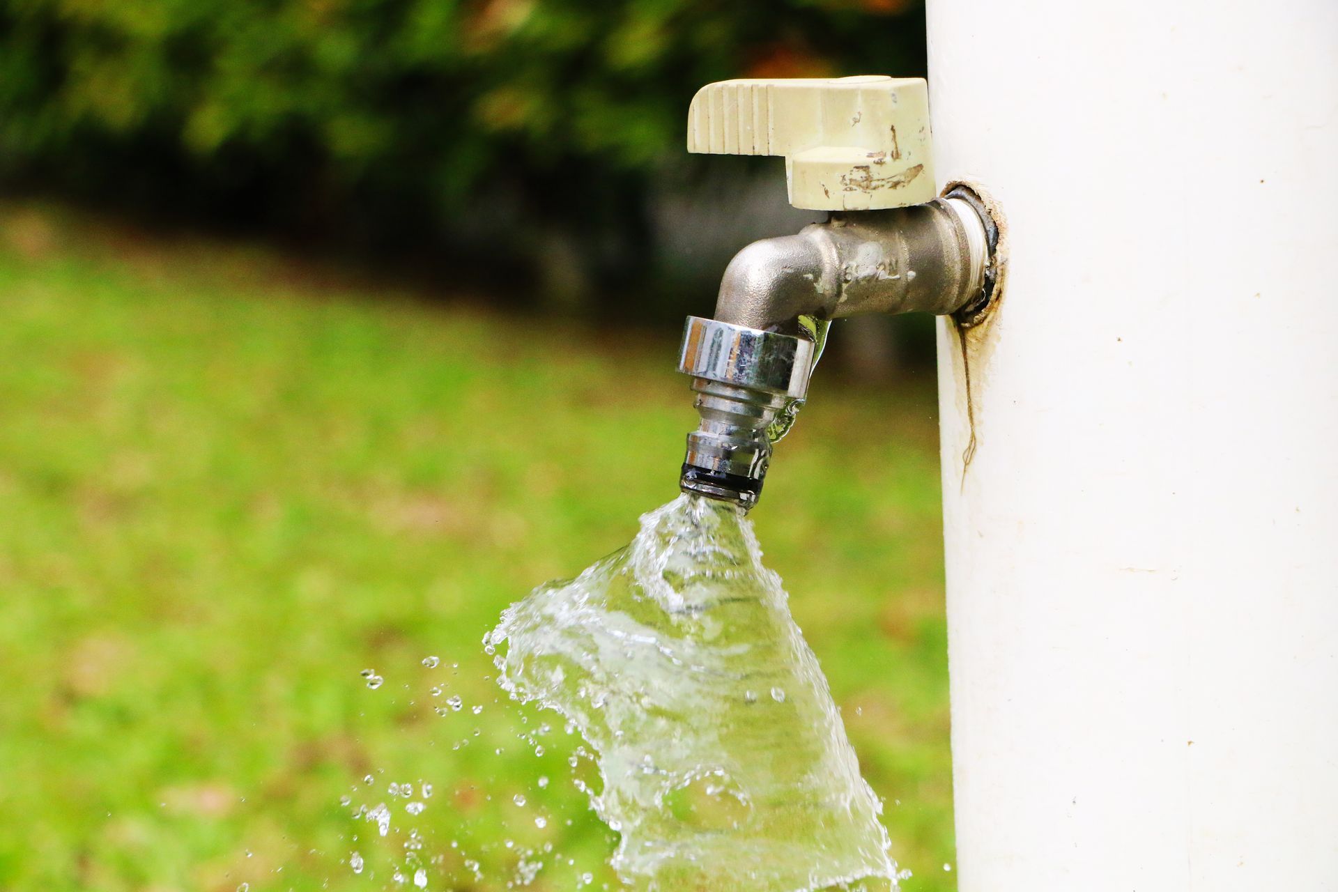 Water spraying from a chrome outdoor faucet attached to a white wall