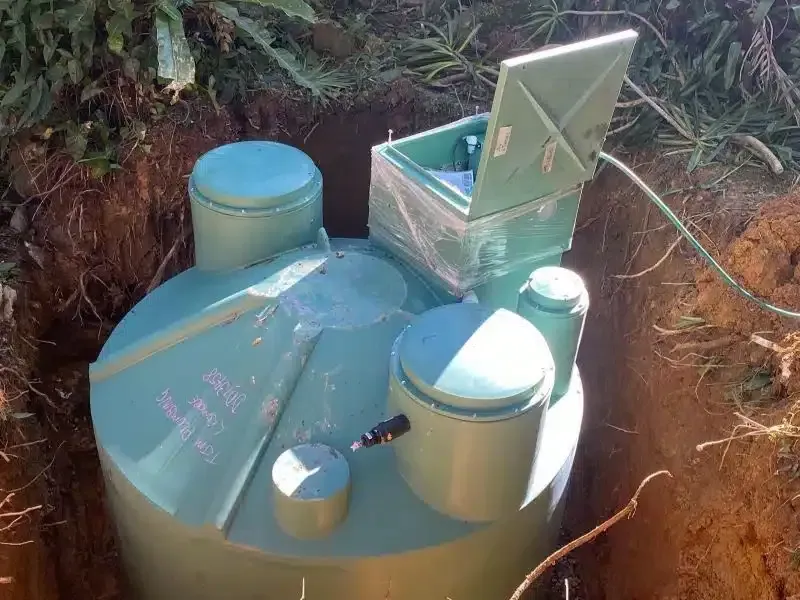 A green septic tank installed in a dug-out pit. The tank is in the ground, with lids visible.