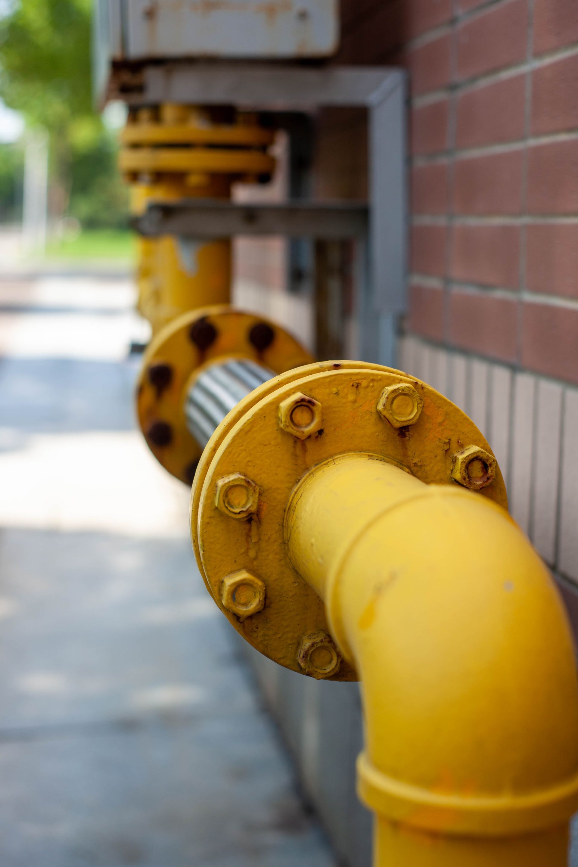 Yellow industrial gas pipes with flanged joints running along a brick wall outdoors