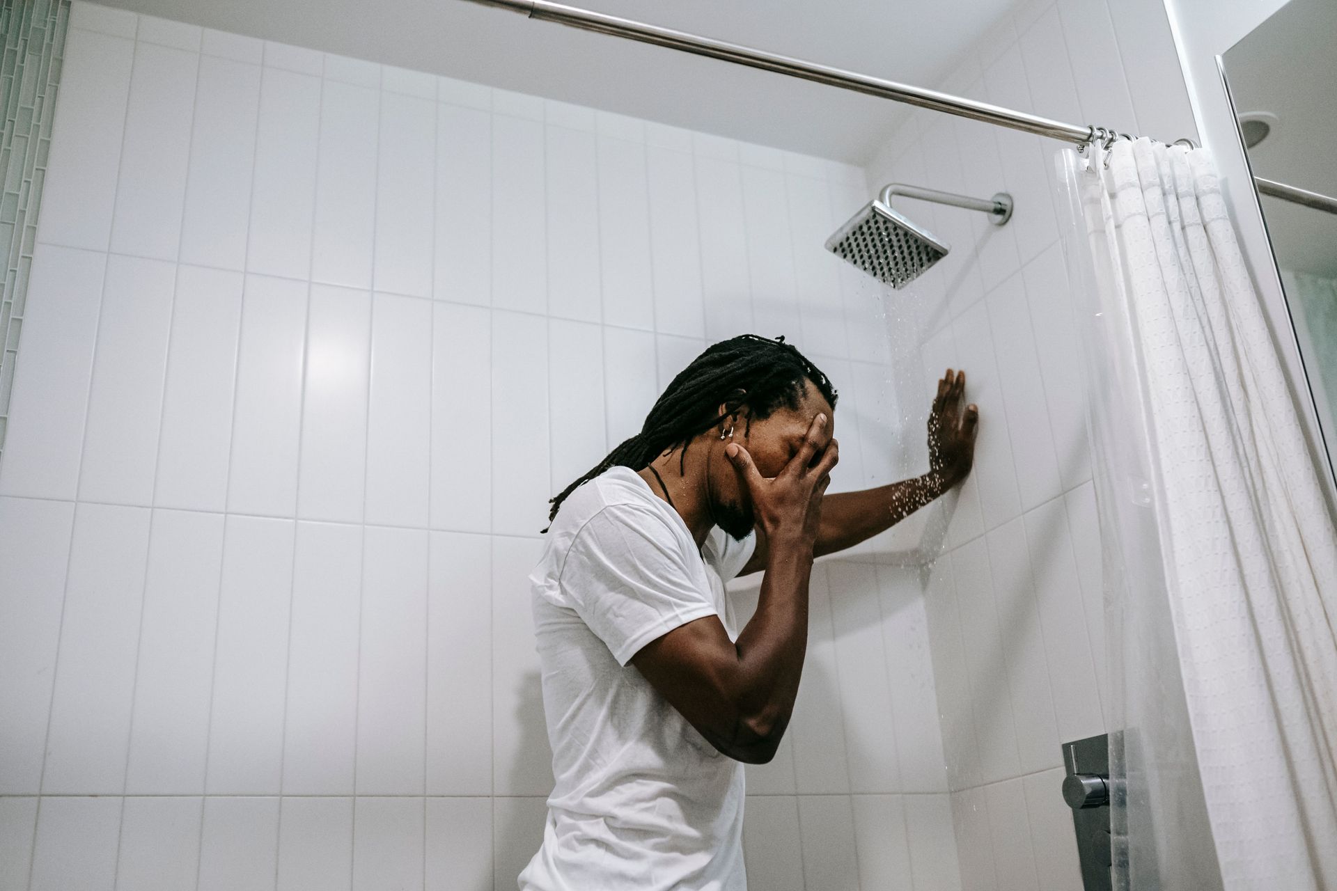Person showering in a tiled bathroom, washing their face under a showerhead.
