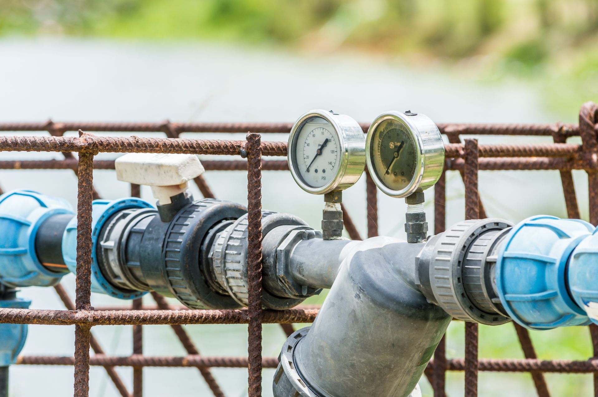 Water pipeline with pressure gauges and valves outdoors, connected by blue and black pipes
