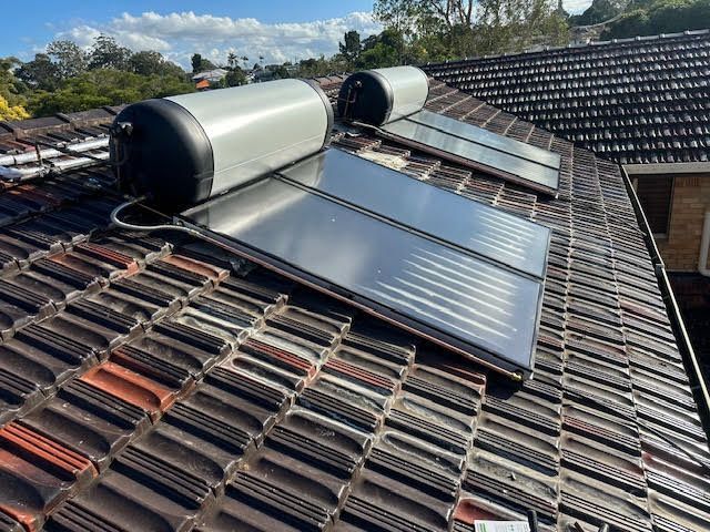 Solar water heating system on a tiled roof, with two panels and two cylindrical tanks.