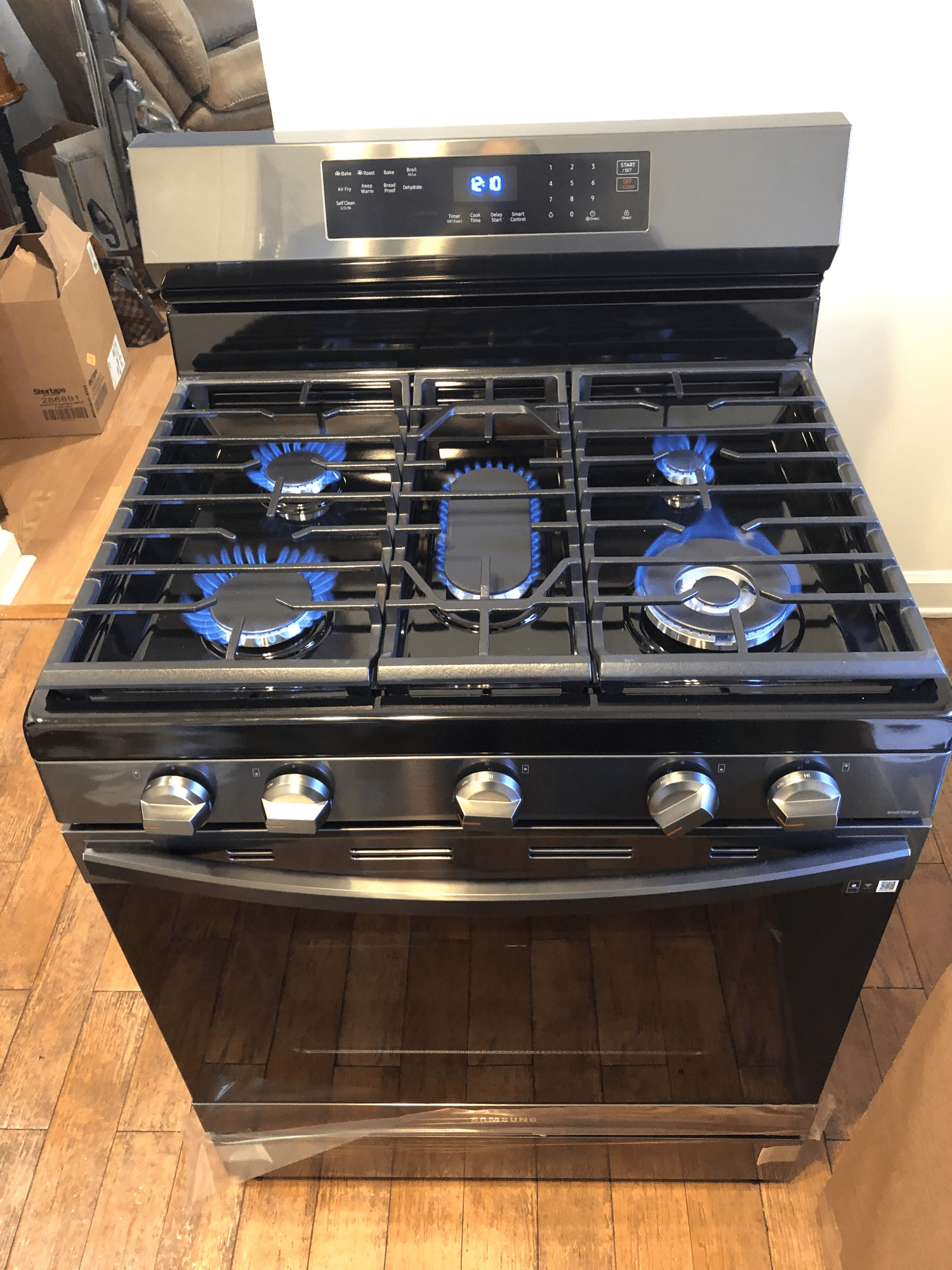 A black gas stove with blue flames is sitting on a wooden floor.