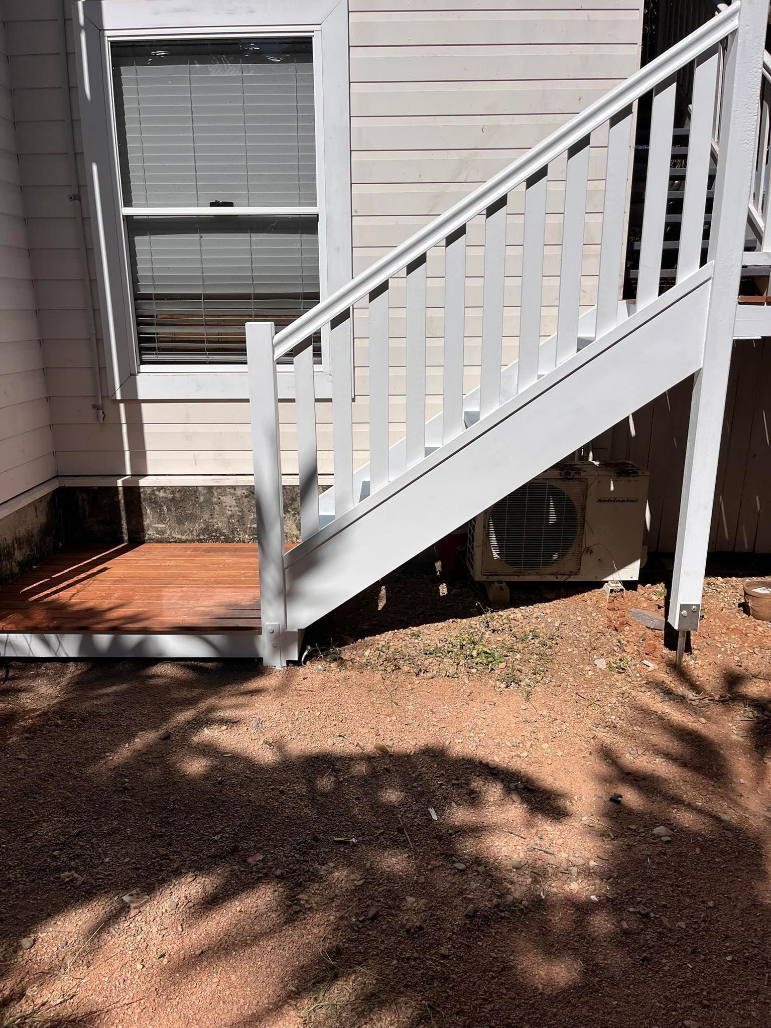 White staircase with railing, attached to a building. Brown gravel ground. AC unit visible.  — Shaun Steenson Building Services in Townsville, QLD