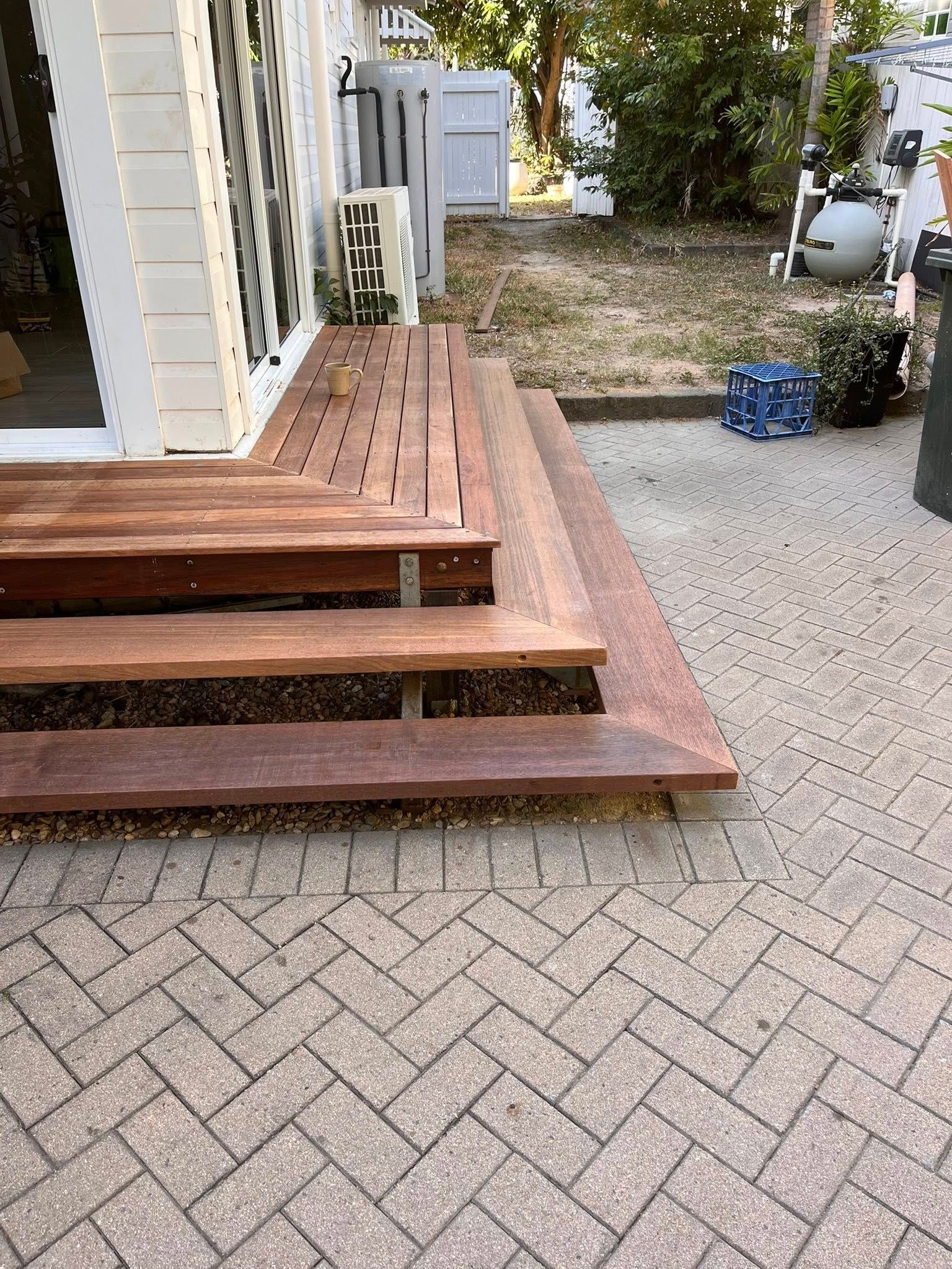 Wooden front steps beside a house, leading to a paved driveway with a small yard and utility equipment nearby. — SS Building Services in Townsville, QLD
