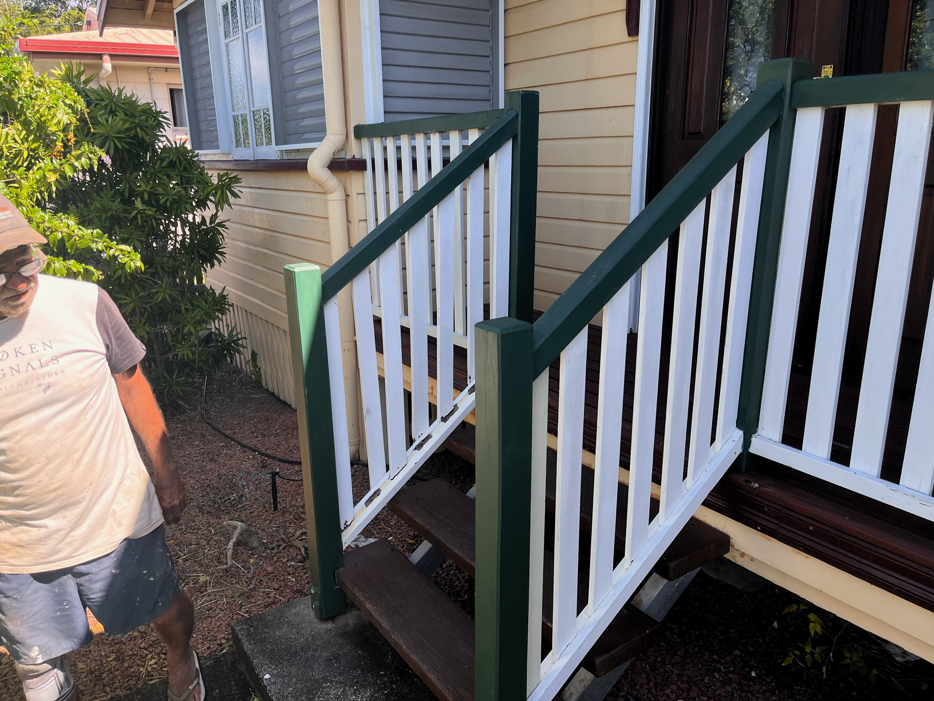 Person Standing Beside a House Porch with White Railings and Dark Green Trim — SS Building Services in Townsville, QLD