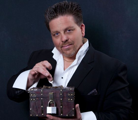 A man in a tuxedo is holding a box with a padlock on it