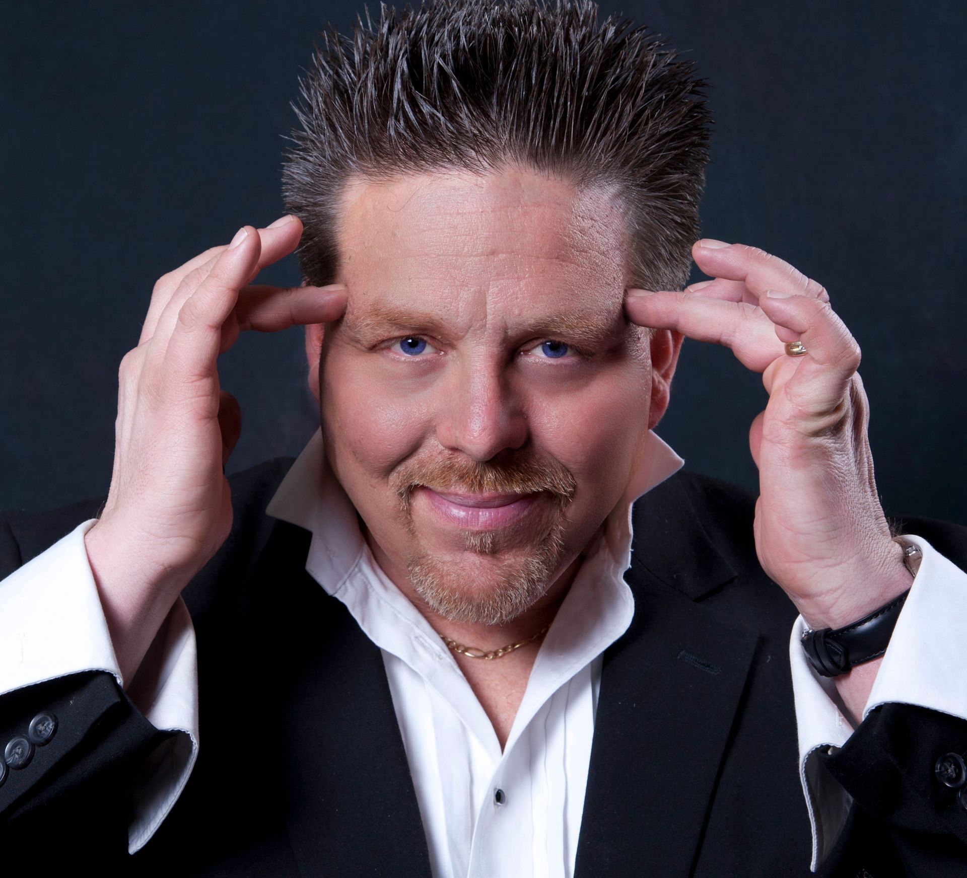 A man in a suit and white shirt is touching his head