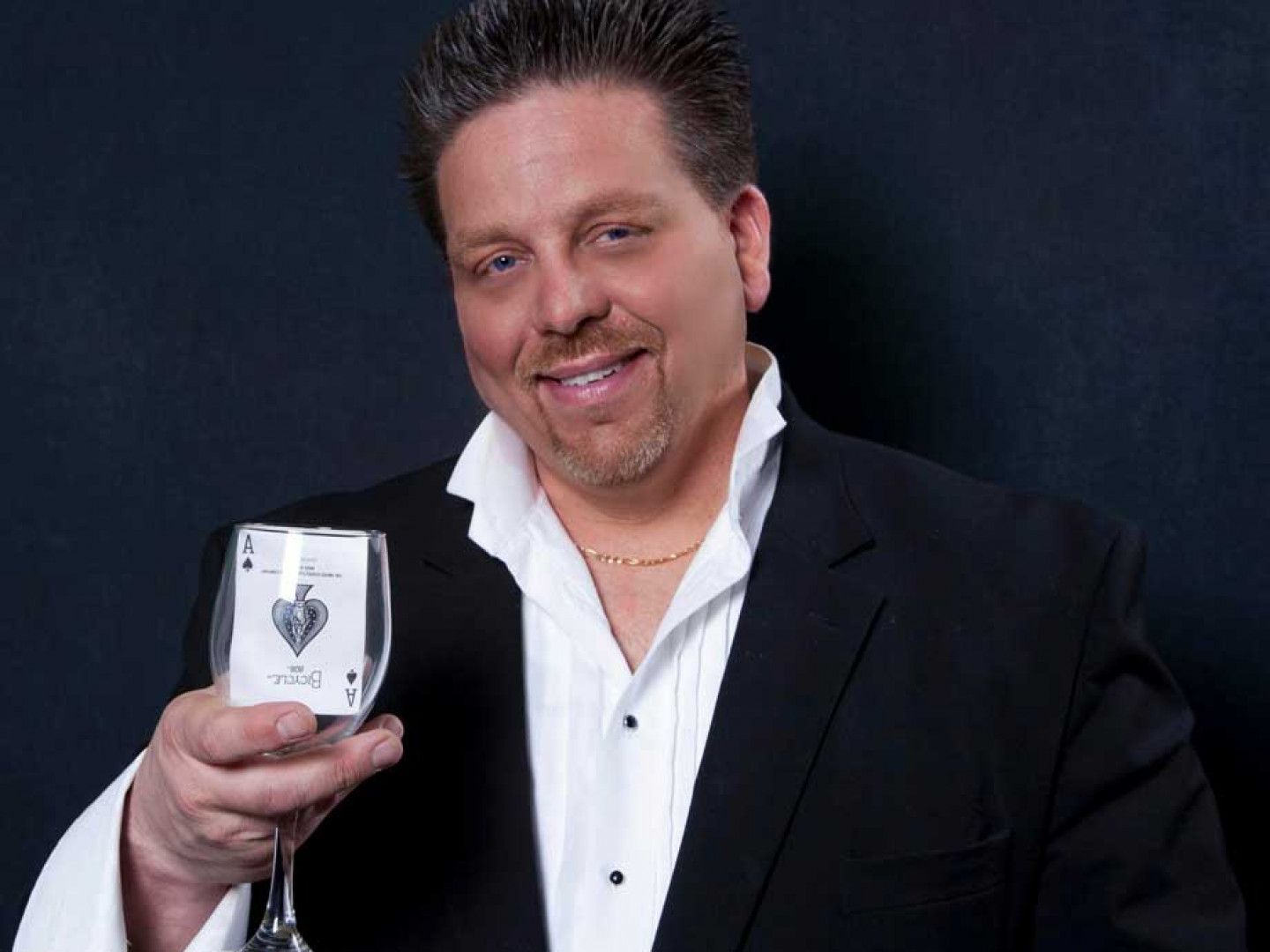 A man in a tuxedo is holding a glass of wine and playing cards