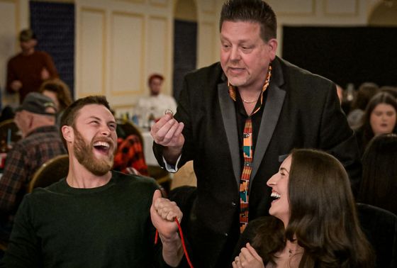 Magician performs a trick with string, entertaining laughing couple at a banquet.