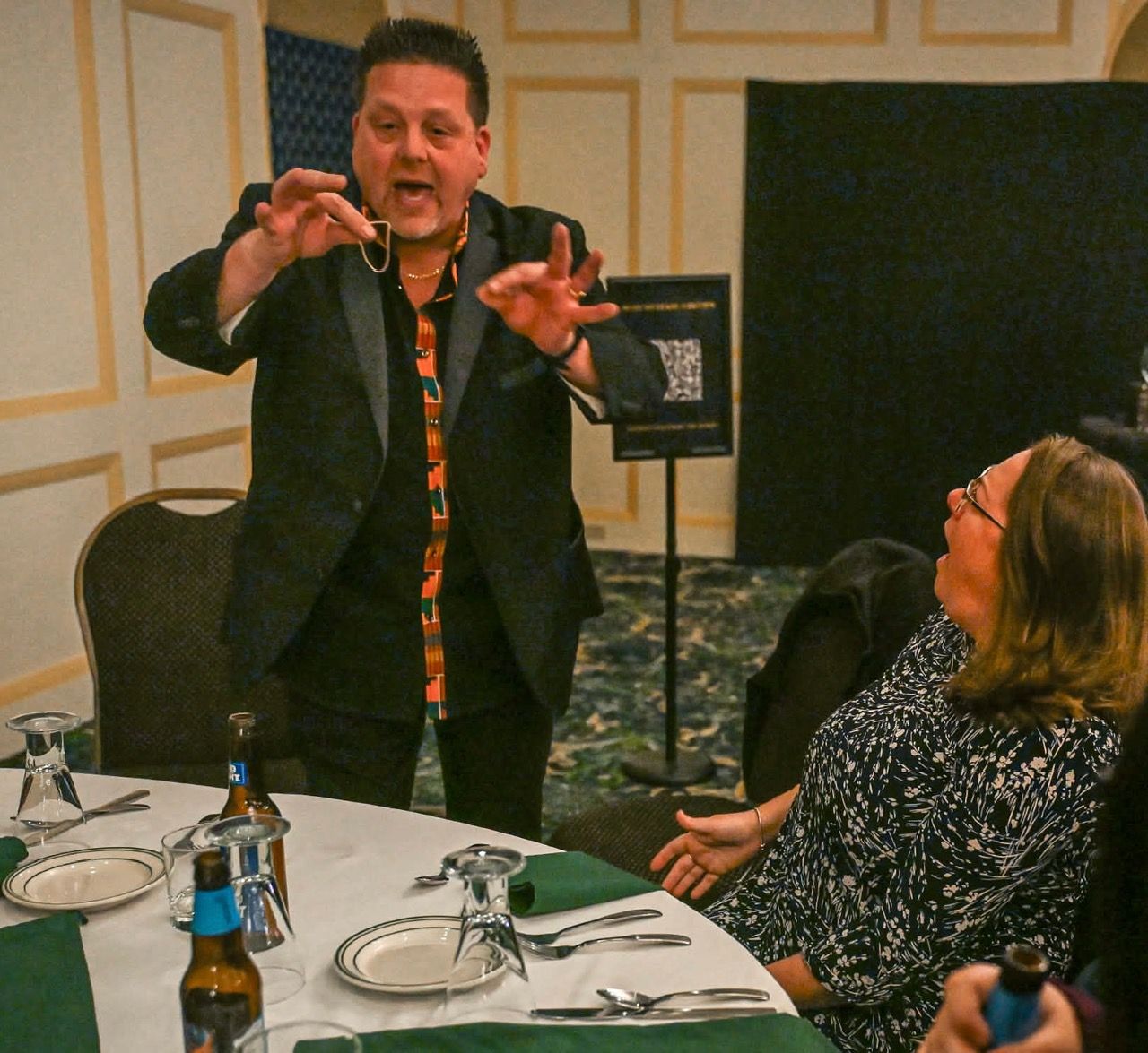 A woman in a purple dress is sitting at a table while a man performs a magic trick.