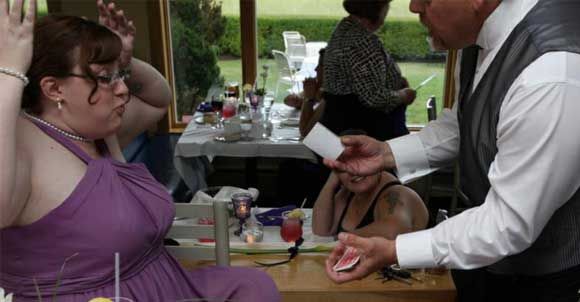 A woman in a purple dress is sitting at a table while a man performs a magic trick.