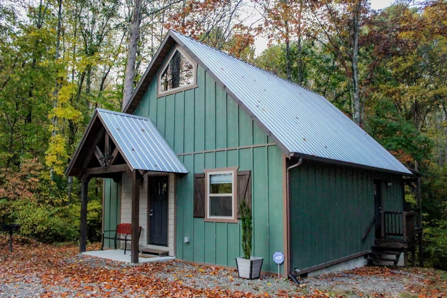 Small green cabin with a blue metal roof in a wooded autumn setting