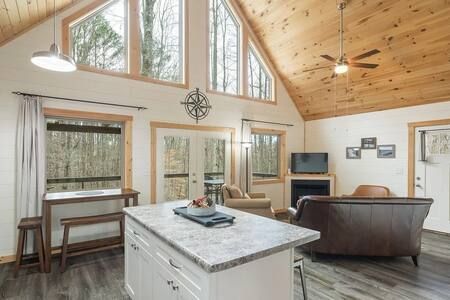 Bright living room with vaulted wood ceiling, large windows, fireplace, and marble kitchen island