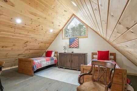 A cozy attic bedroom with wood-paneled walls, twin beds, a cabinet, and red accents.