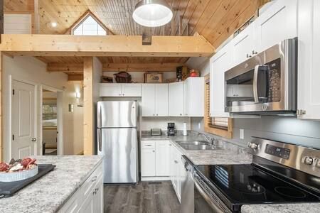 Bright modern kitchen with stainless steel appliances, white cabinets, marble island, and wood vaulted ceiling