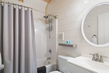 Bright white bathroom with a round mirror, tub shower curtain, and sink counter.