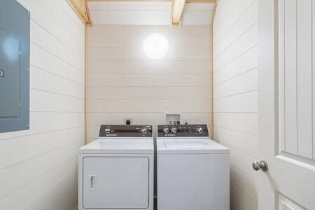 Small laundry room with a washer, dryer, and bright wall light between white paneled walls