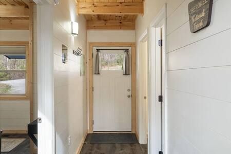 Narrow hallway with white walls, wood ceiling, and a white front door at the end