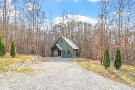 Small green house with a gravel driveway, surrounded by bare trees under a blue sky.