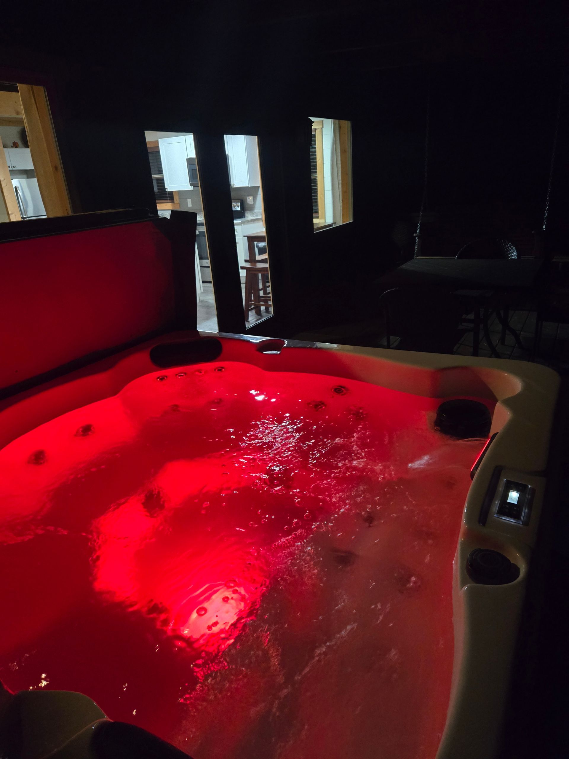Red-lit indoor hot tub with bubbling water, beside a dark room with windows.