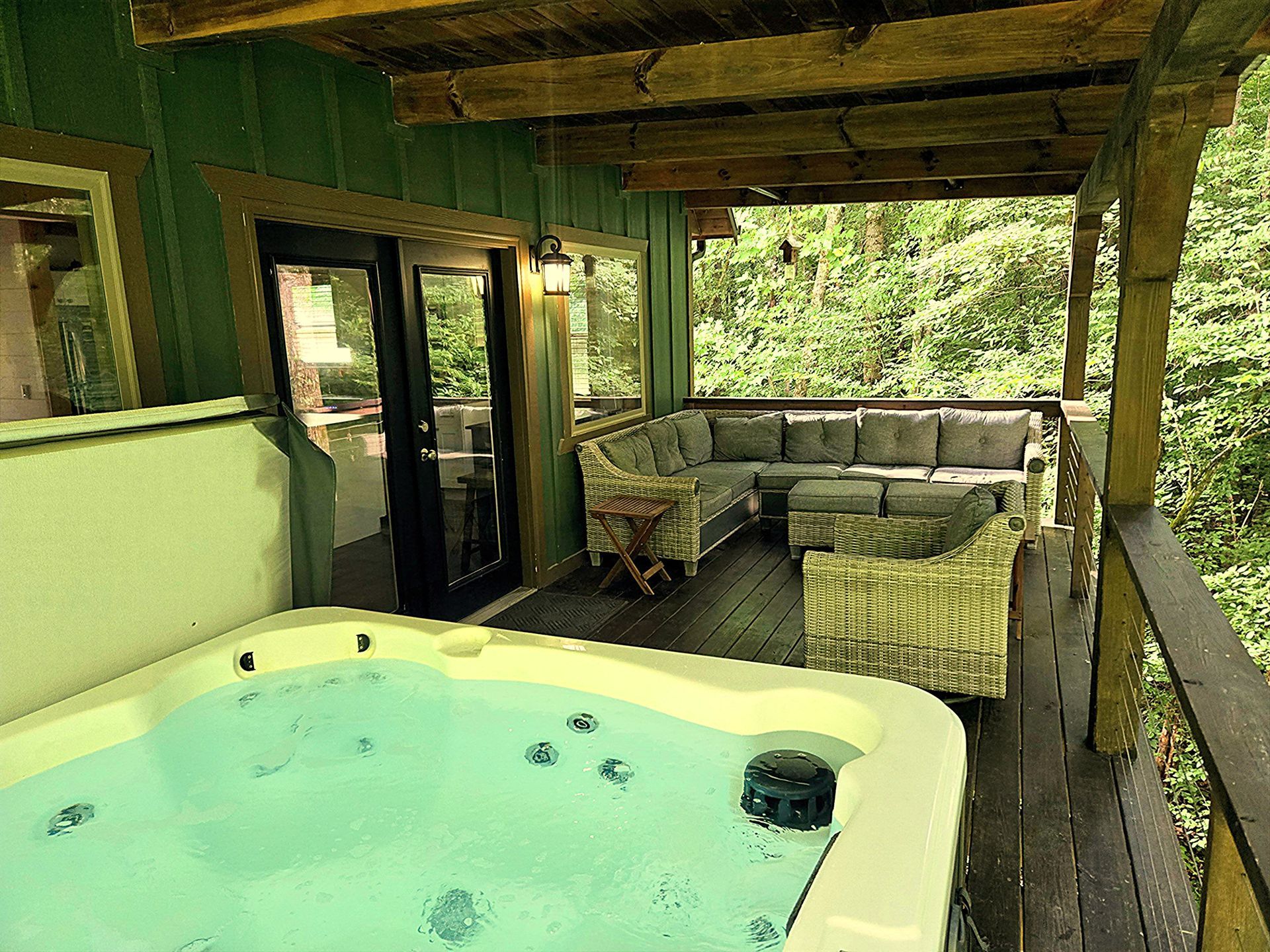 Covered outdoor hot tub on a wooden deck with green walls and a forest view