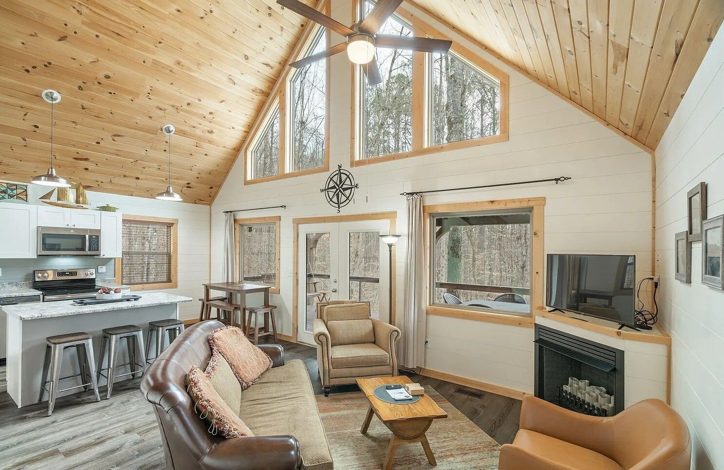 Cozy cabin living room with vaulted wood ceiling, leather chair, TV, fireplace, and kitchen area
