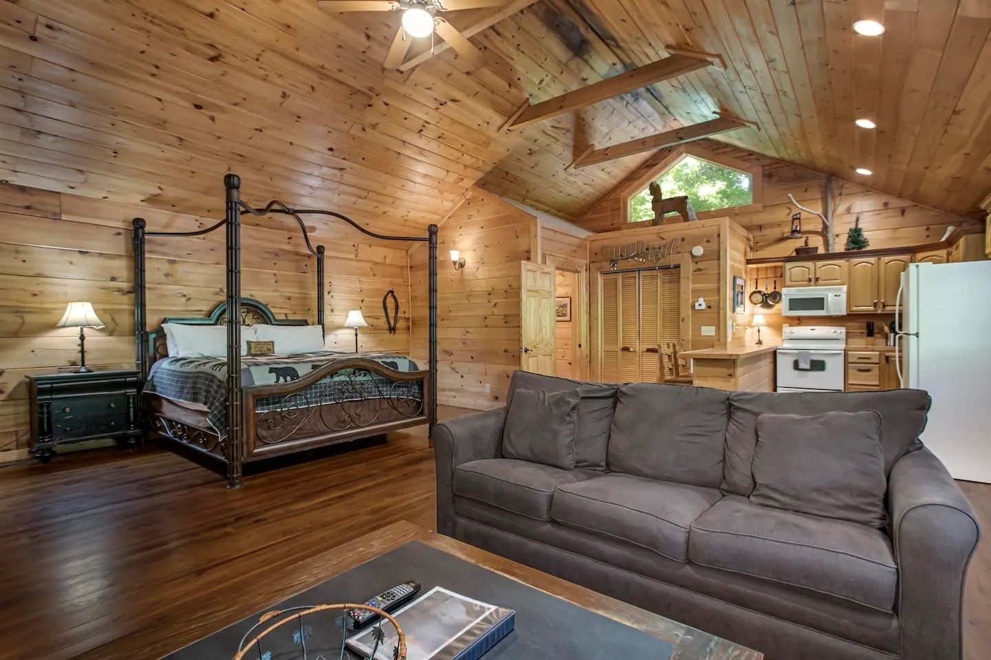 Wooden loft bedroom with a canopy bed, gray sofa, and kitchen area in a cozy cabin interior