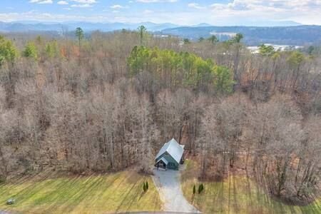 Small white house at the edge of a wooded hill, with a driveway and mountains in the distance.