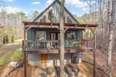 Wooden A-frame cabin with a front deck, surrounded by trees in a wooded setting.