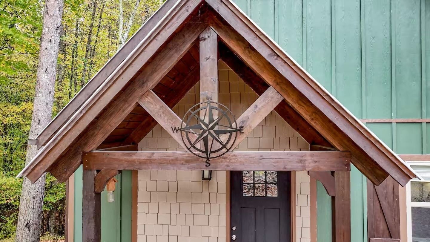 Wooden church entrance with a steep gabled roof and hanging lantern, framed by trees and green siding.