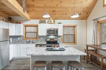 Bright kitchen with white cabinets, gray island, wood ceiling, and dining table by the window.