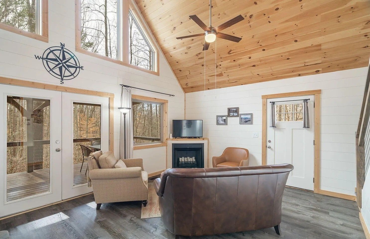 Cozy living room with vaulted wood ceiling, leather sofa, armchair, fireplace, and large windows