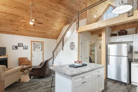 Cozy open-concept cabin living room with wood ceiling, kitchen island, and stainless-steel fridge.