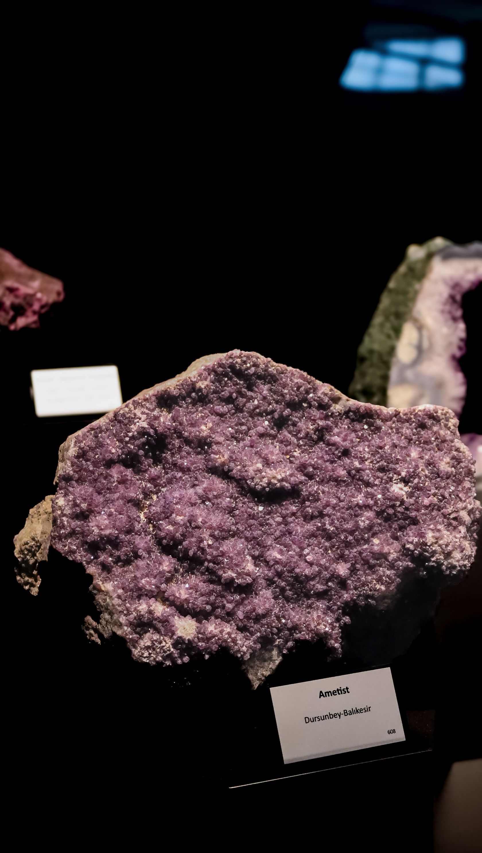 Purple crystalline mineral specimen displayed on a dark museum exhibit background