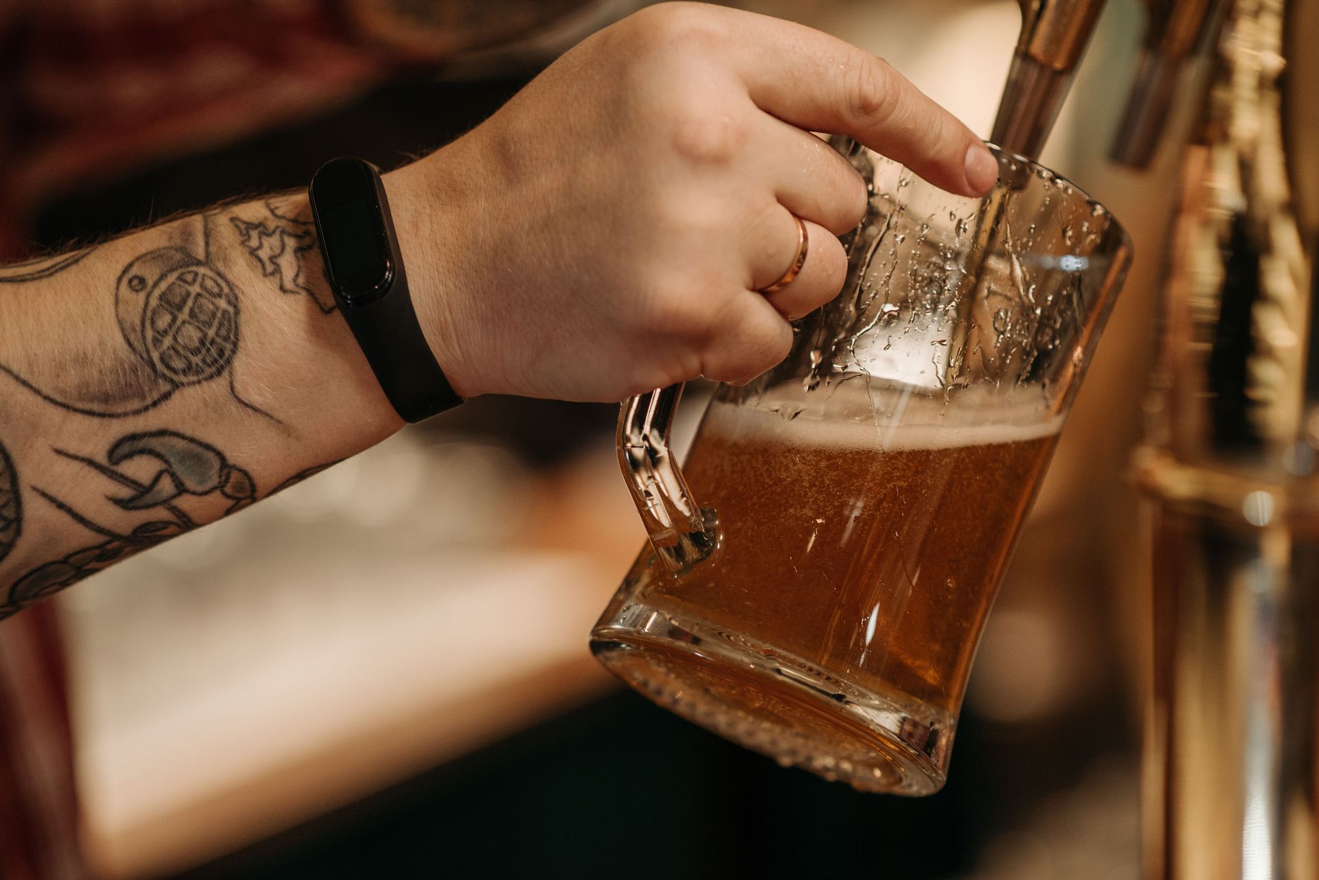 Tattooed hand holding a beer mug being filled from a tap