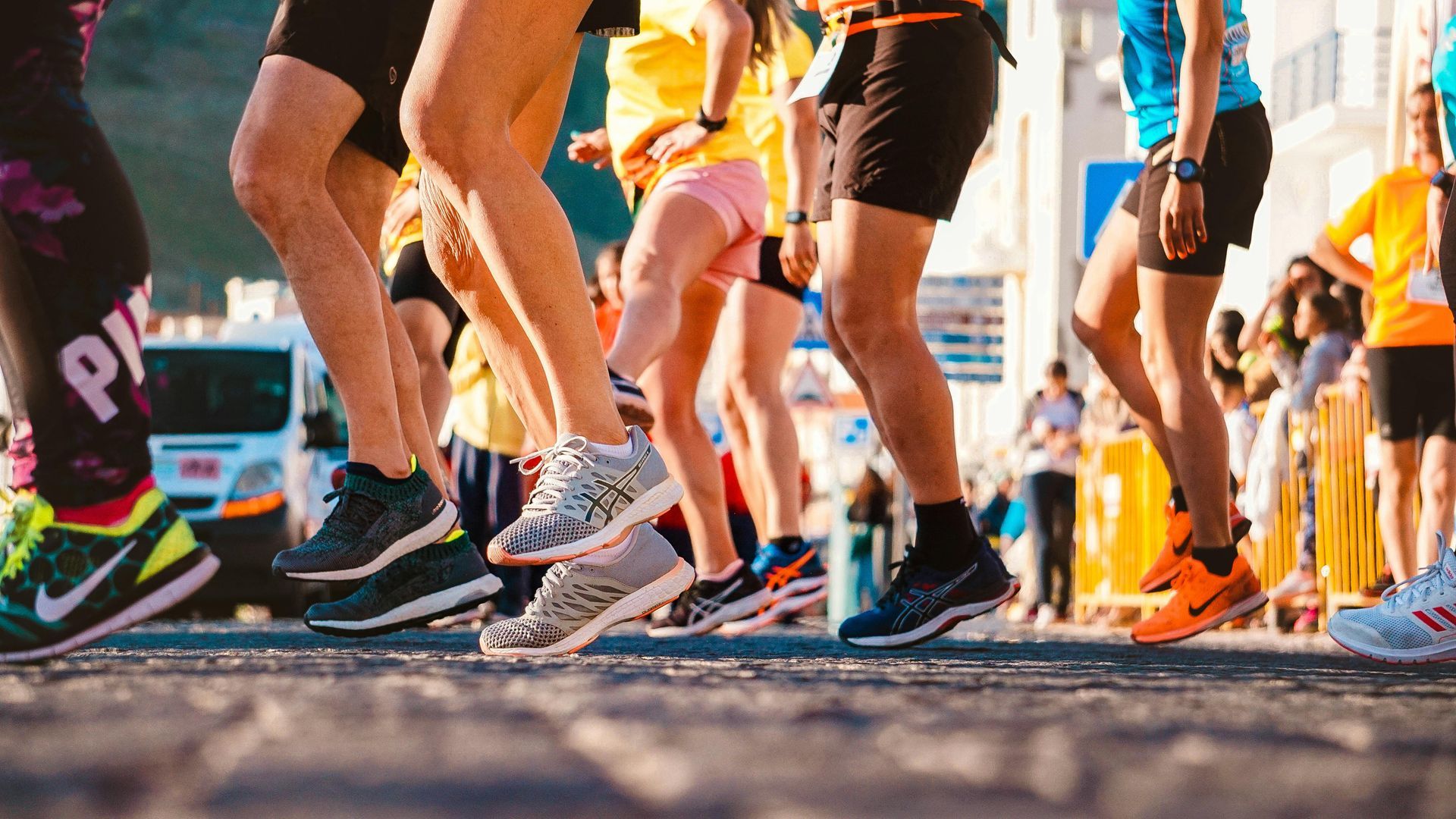 Runners in a race, legs and feet visible, various shoes and outfits, on a paved road.