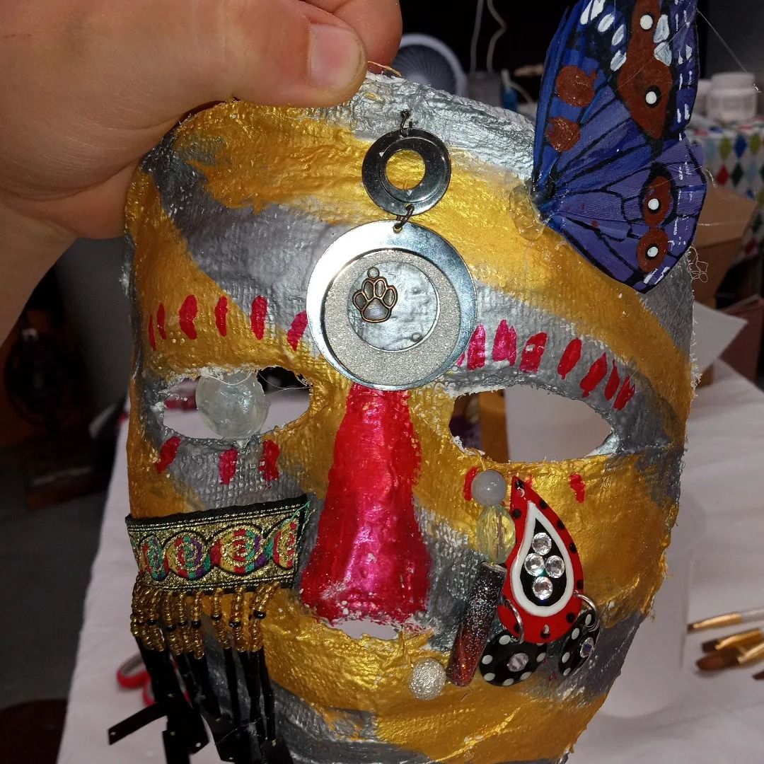Mask, gold and silver, with butterfly, jewel and red nose. Held by hand.