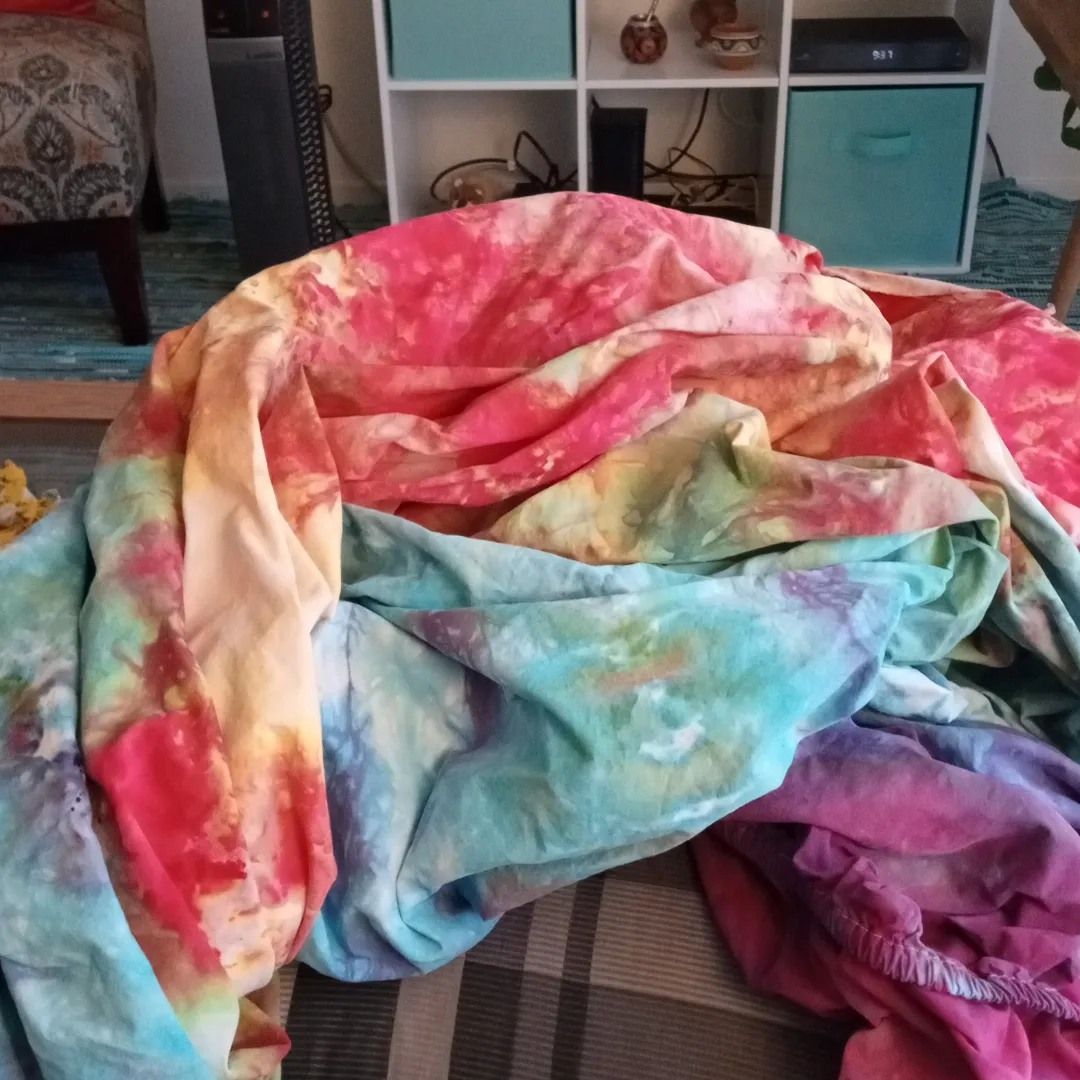 Colorful tie-dye fabric spread on a patterned surface; red, pink, blue, and yellow hues dominate.