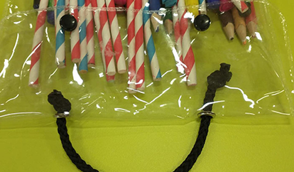 Clear bag with straw-like colorful pencils and black handles on a yellow background.