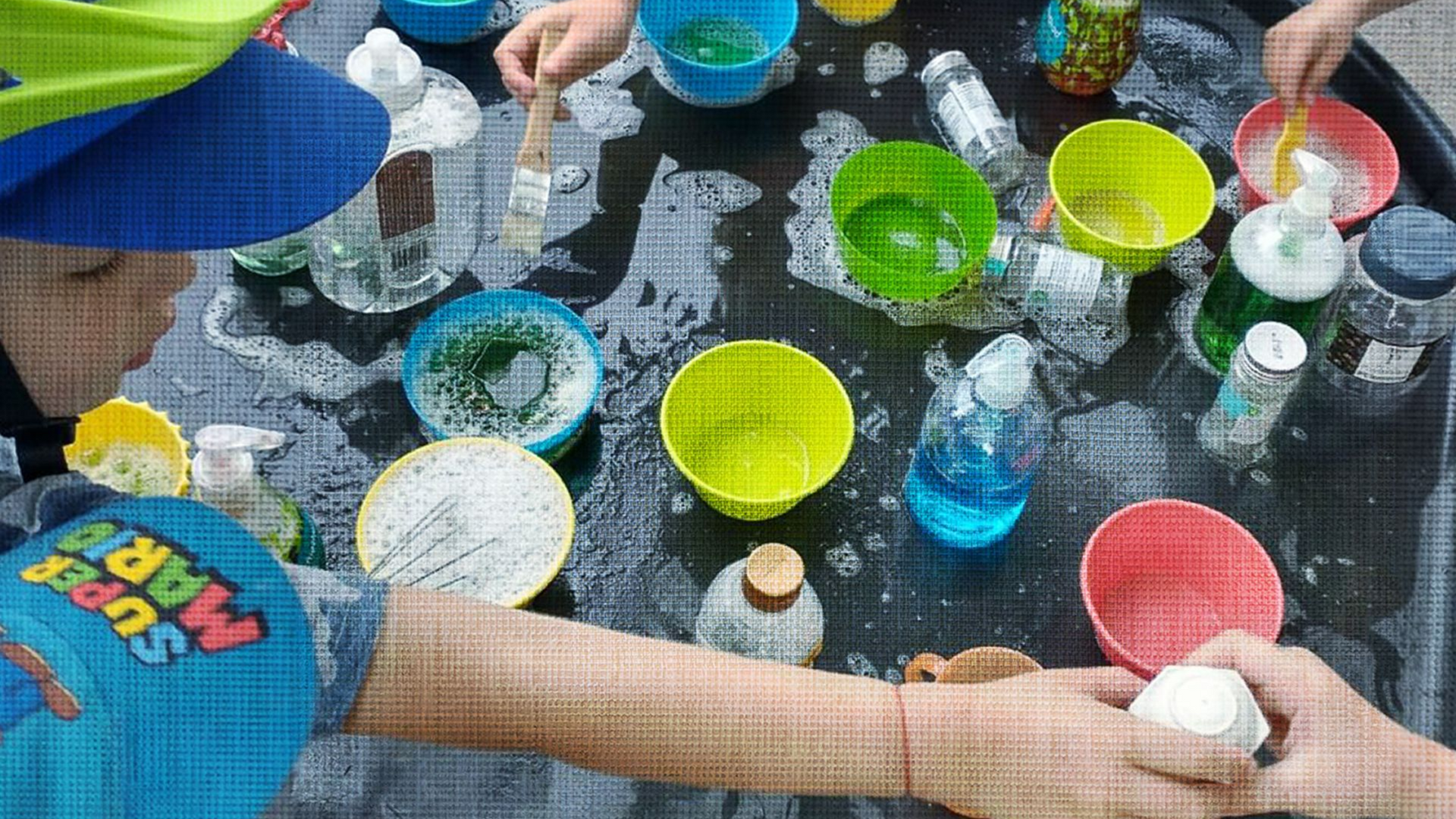 Children playing with colorful bowls and liquids on a black table.
