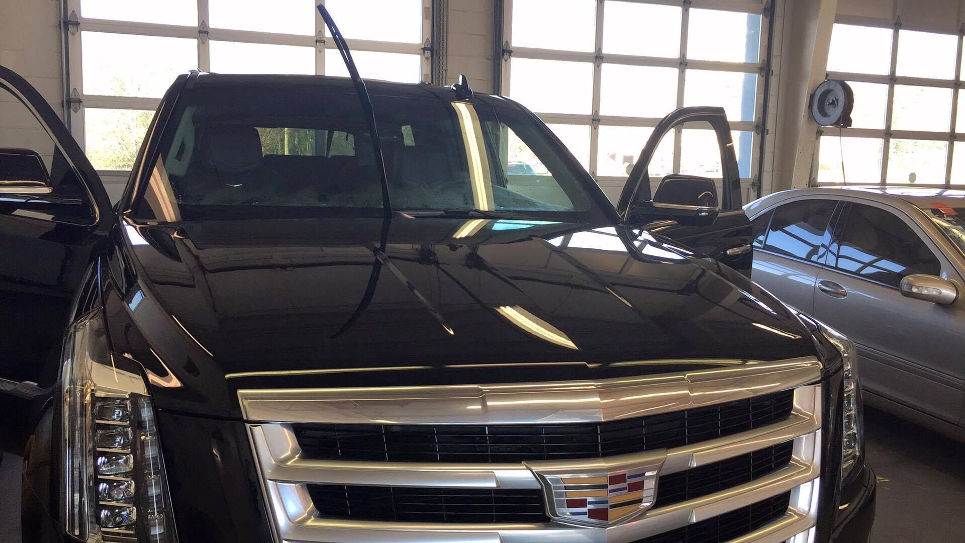Black Cadillac SUV with open doors in a garage, next to another car.