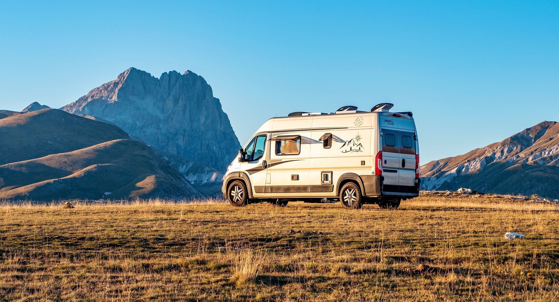 A rv is parked in a field with mountains in the background.