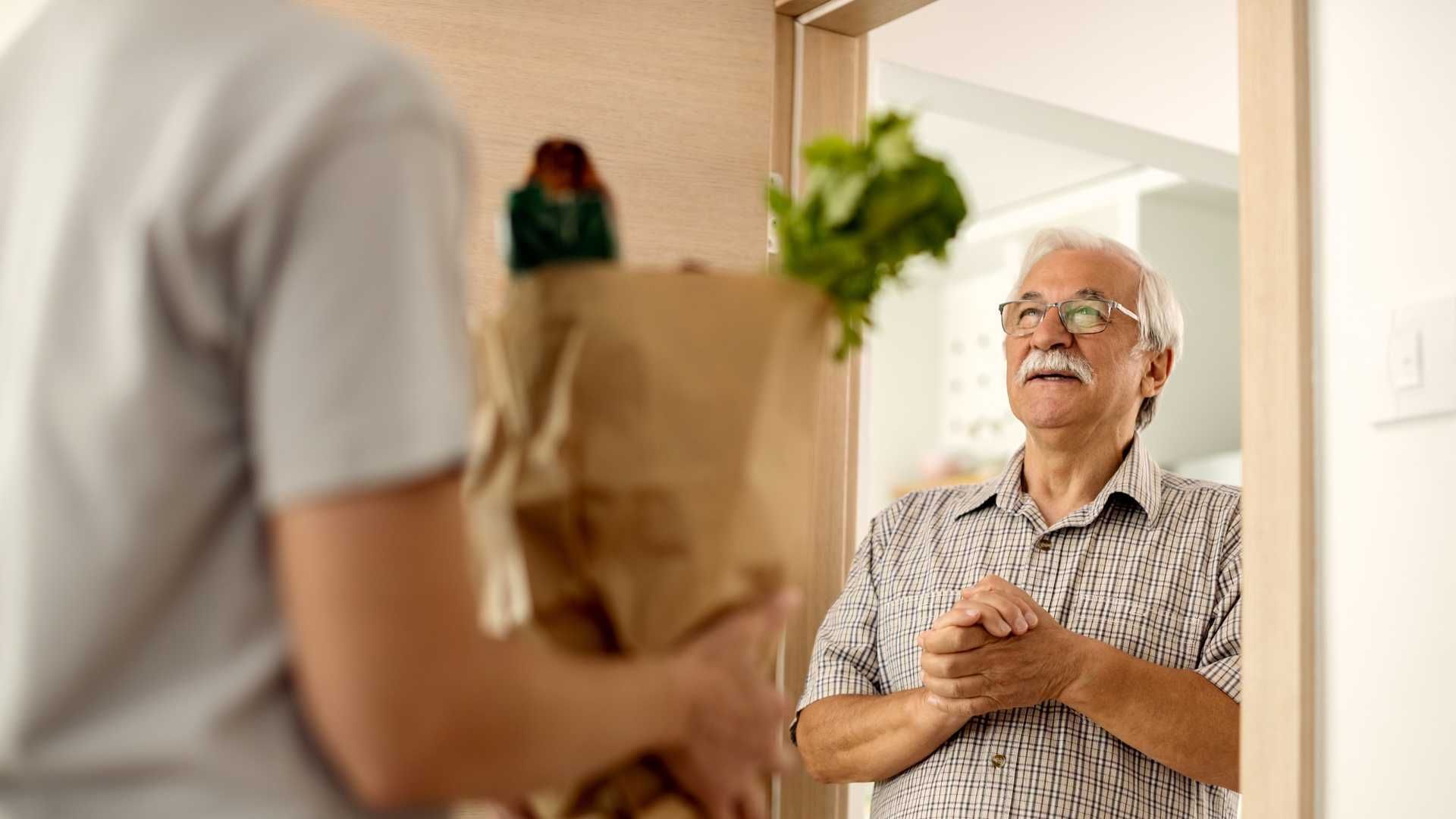 A man is standing in front of a door holding a bag of groceries.